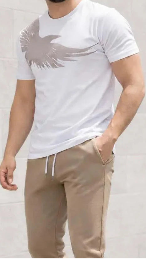 Man wearing a white t-shirt with a logo and beige pants against a light gray background