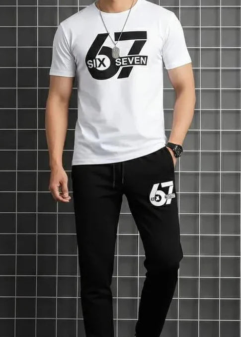 Person wearing a white t-shirt with a logo and black pants with numbers, standing against a tiled wall.