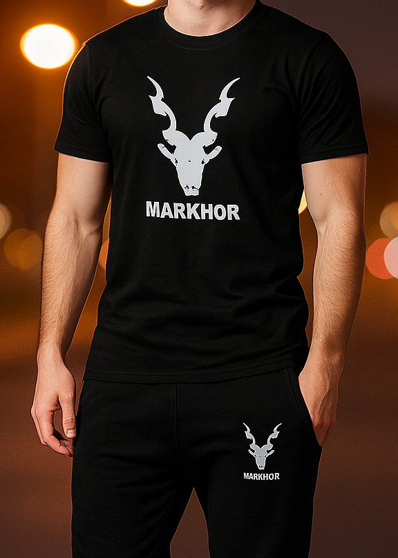 Person wearing a black t-shirt and pants with 'MARKHOR' logo on a blurred warm-toned background