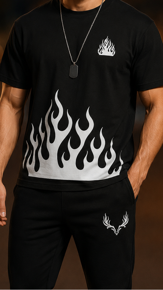 A man wearing a black short-sleeve t-shirt with a white flame graphic across the lower front and matching black pants, standing against a dark, blurred background with warm bokeh lights.